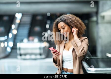 Junge Frau mit Handy und Ohrstöpsel an der U-Bahn-Station Stockfoto