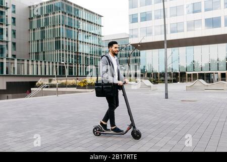 Legerer junger Geschäftsmann, der in der Stadt mit einem Elektro-Roller unterwegs ist Stockfoto