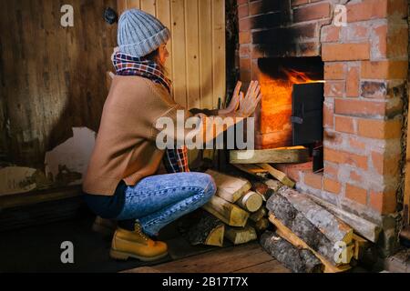 Frau hockend vor dem Kamin wärmen ihre Hände Stockfoto