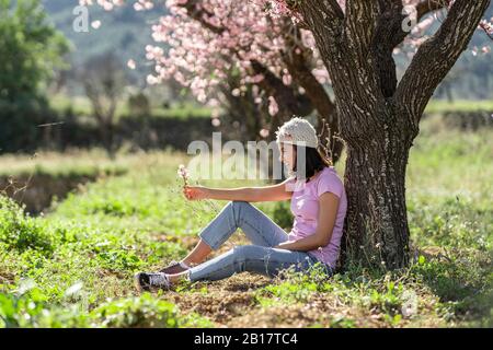 Glückliches Teenager-Mädchen lehnt sich an Mandelbaum Blick auf Zweig der Mandelblüten Stockfoto