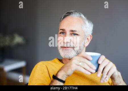 Porträt eines lächelnden, entspannten, reifen Mannes zu Hause mit einer Tasse Kaffee Stockfoto