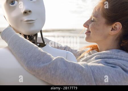 Glückliche Frau, die den Roboter am Strand umarmte Stockfoto
