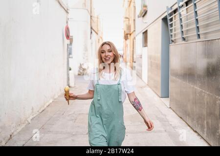 Porträt der glücklichen jungen Frau mit Eiszapfen zu Fuß entlang einer Gasse Stockfoto