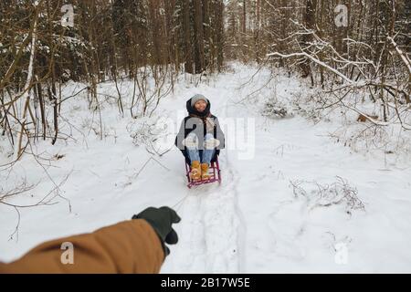 Die Hand des Mannes zieht Frau auf einem Schlitten sitzen Stockfoto