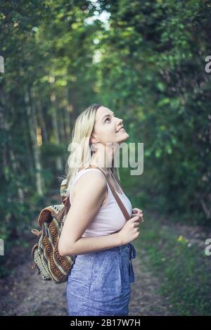 Lächelnde junge Frau mit Rucksack im Wald, die etwas beobachtet Stockfoto