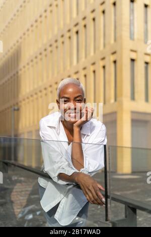 Attraktive Geschäftsfrau, die sich an Geländer in der Stadt lehnt Stockfoto