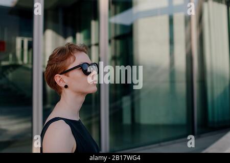 Elegante rothaarige Frau mit Sonnenbrille in der Stadt, Porträt Stockfoto
