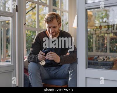 Mann hält Kamera zu Hause im Sonnenraum Stockfoto