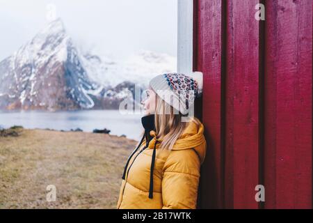 Lächelnder Tourist lehnt eine Hütte in Hamnoy, Lofoten, Norwegen ab Stockfoto