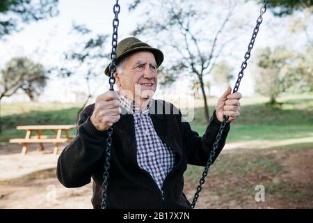 Alter Mann schwingt auf Spielplatz im Park Stockfoto