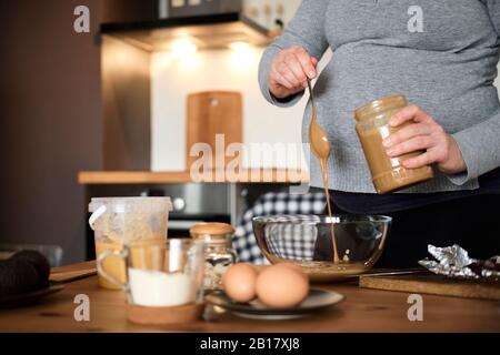 Schwangere Frau macht zu Hause gesunden Kuchen mit Tahini, Walnüssen und dunkler Schokolade Stockfoto