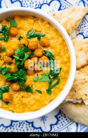 Veganes Linsencurry mit roten Linsen, Süßkartoffeln, Spinat, gerösteter Kurkuma, Kichererbsen, mit Limettensaft und Koriander und Naanbrot Stockfoto