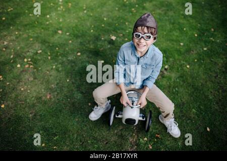 Kleiner Junge, der Spaß hat und Oldtimerwagen im Garten fährt Stockfoto