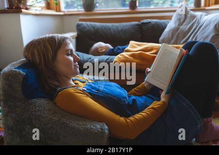 Frau liest Buch im Wohnzimmer mit kleinem Sohn schlafend Stockfoto