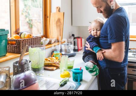 Mann in der Küche, der Essen zubereitete und seinen Sohn kuschte Stockfoto