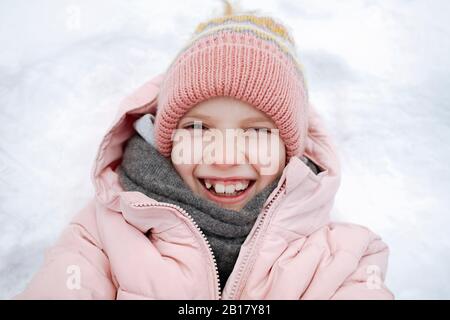 Porträt des glücklichen Mädchens, das auf Schnee liegt Stockfoto