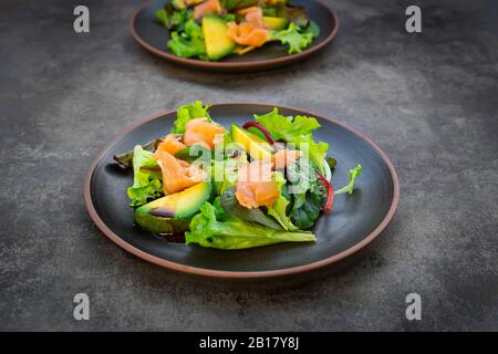 Teller mit grünem Salat mit Maissalat, Rucola, Spinat, rotem Blattsalat, Rote-Bete-Blätter, Avocado, Lachsfleisch und Balsamico-Essig Stockfoto