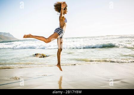 Glückliche junge Frau am Strand springen Stockfoto
