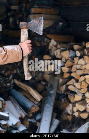 Hand des Mannes hält Axt vor Stapel von Brennholz im Winter Stockfoto