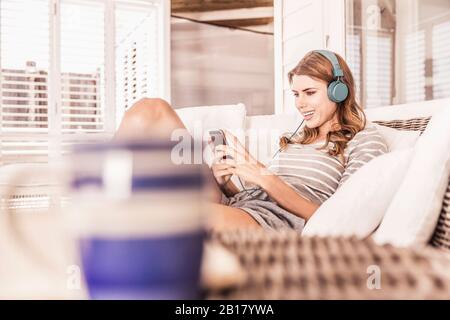 Junge Frau auf einer Veranda mit Smartphone und Kopfhörer entspannen Stockfoto
