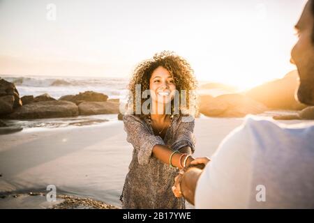 Glückliches Paar, das bei Sonnenuntergang am Strand die Hände hielt Stockfoto