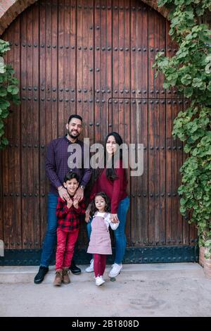 Porträt einer lächelnden Familie mit zwei Kindern, die am Holztor stehen Stockfoto