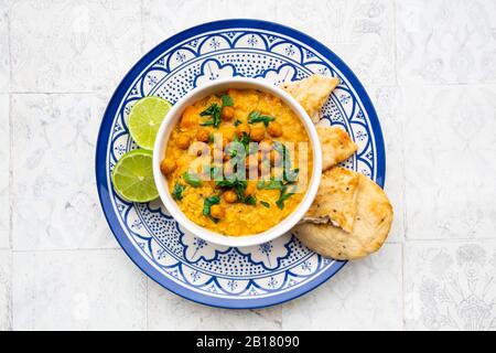 Veganes Linsencurry mit roten Linsen, Süßkartoffeln, Spinat, gerösteter Kurkuma, Kichererbsen, mit Limettensaft und Koriander und Naanbrot Stockfoto