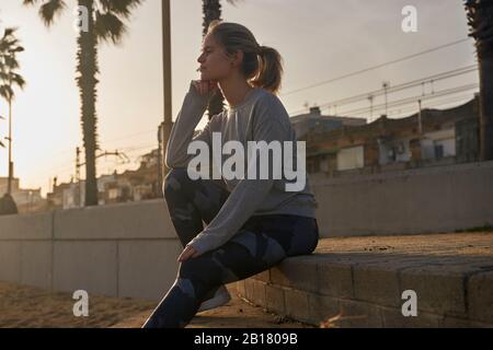 Sportliche junge Frau, die bei Sonnenuntergang auf der Promenade am Strand eine Pause einlegen kann Stockfoto