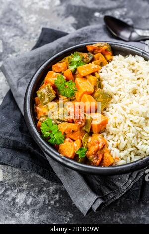 Curry mit Süßkartoffeln, Karotten, Pilzen, Zucchini, Zuckererbsen, Tomaten, Petersilie und Reis in der Schüssel Stockfoto