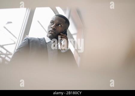 Porträt des jungen Geschäftsmannes vor dem Fenster am Telefon Stockfoto
