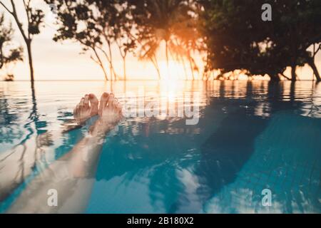 Beine der Frau im Infinity-Pool bei Sonnenuntergang, Nai Thon Beach, Phuket, Thailand Stockfoto