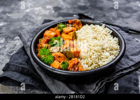 Curry mit Süßkartoffeln, Karotten, Pilzen, Zucchini, Zuckererbsen, Tomaten, Petersilie und Reis in der Schüssel Stockfoto