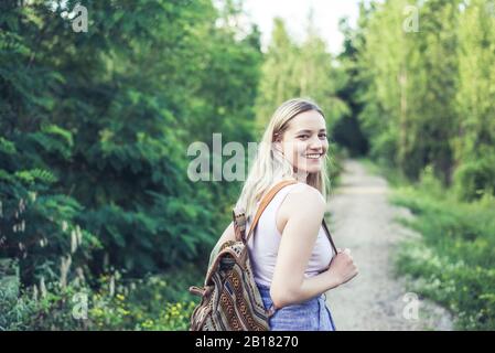 Porträt einer lächelnden jungen Frau mit Rucksack auf Waldbahn Stockfoto