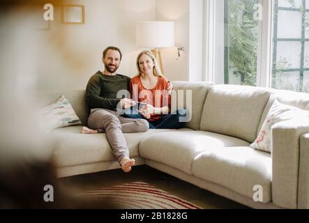 Paare sitzen zu Hause auf dem Sofa und verwenden ein digitales Tablet Stockfoto