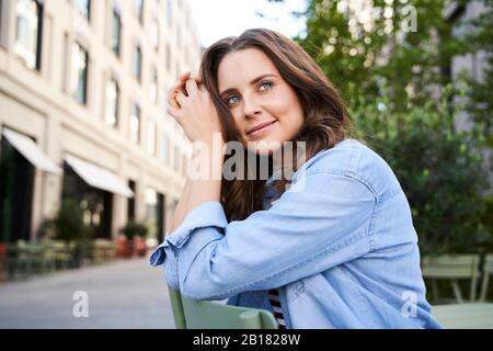 Porträt von lächelnden Brünette Frau auf einem Stuhl in der Stadt sitzen Stockfoto