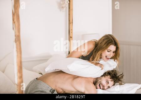 Unbeschwerte junge Paar mit einem Kopfkissen Kampf im Bett Stockfoto