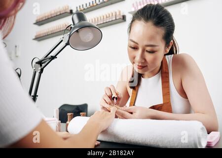 Schöner junger asiatischer Manikurist, der im Schönheitssalon arbeitet und nagellack aufwendet Stockfoto