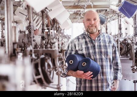 Porträt des Mannes, der Baumwollrollen in einer Textilfabrik hält Stockfoto