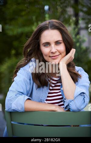 Porträt von lächelnden Brünette Frau auf einem Stuhl in der Stadt sitzen Stockfoto