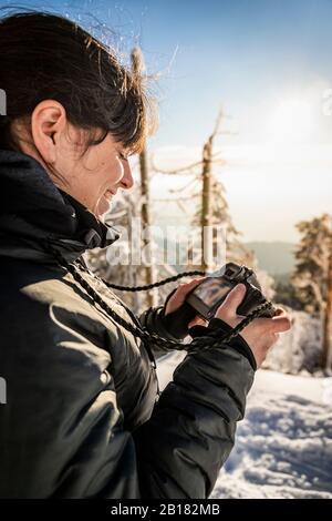 Smling Woman überprüft die Anzeige der Kamera im Winter in Hornisgrinde, Schwarzwald, Deutschland Stockfoto