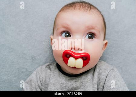 Portrait von Baby Mädchen mit großen Zähnen Schnuller auf grauen Decke liegen Stockfoto