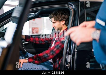 Junger Mann sitzt im Auto im Autohaus Stockfoto