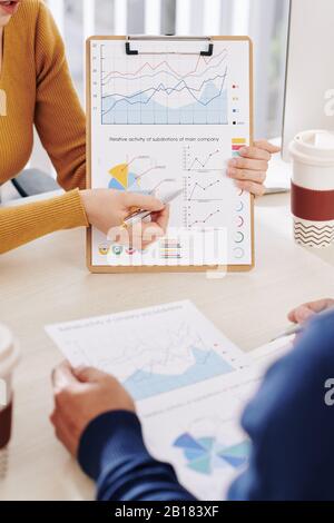 Zugeschnittenes Bild der jungen Geschäftsfrau, die die Zwischenablage mit einem Finanzdiagramm zeigt und Informationen mit Kollegen diskutiert Stockfoto