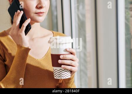 Das Bild einer ernsthaften jungen Geschäftsfrau, die eine große Tasse Kaffee trinkt und telefoniert Stockfoto