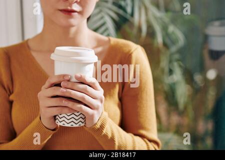 Große Tasse leckeren Kaffees in den Händen junger Frau im warmen Senfpullover Stockfoto