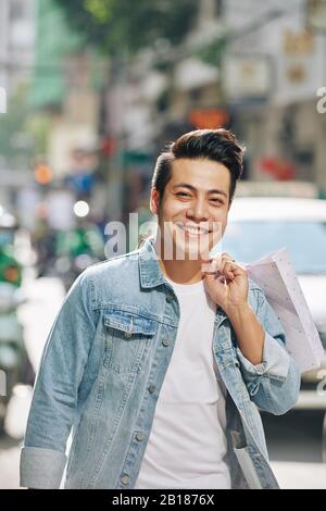 Porträt eines jungen, gutaussehenden Vietnamesen, der mit Einkaufstaschen draußen spazieren ging Stockfoto