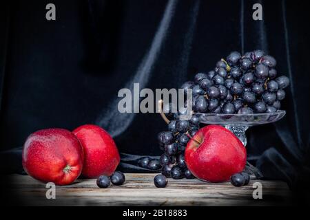 Stillleben von roten Äpfeln und schwarzen Trauben auf einer Holzoberfläche und auf schwarzem Grund Stockfoto