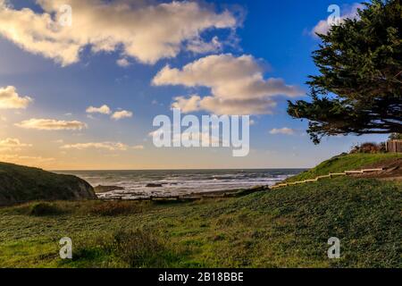 Blick auf den Pazifischen Ozean und den Nordkalifornischen Strand über einen grünen Hügel in Moss Beach bei San Francisco, an einem bewölkten Tag vor Sonnenuntergang Stockfoto