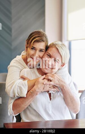 Porträt einer lächelnden jungen hübschen Frau, die ihre hochzufriedene Mutter von hinten umarmte Stockfoto