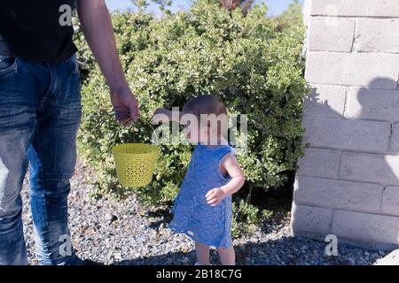 Ein Baby feiert ihr erstes Ostern. Sie läuft kaum und genießt ihre erste Ostereierjagd. Stockfoto